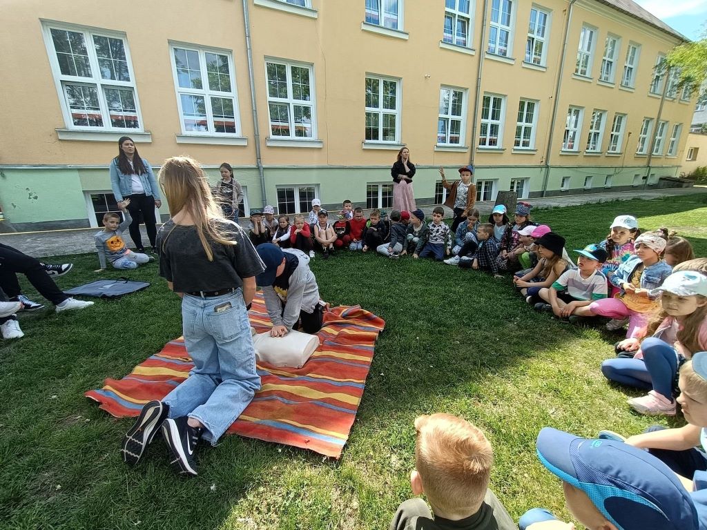 Dzieci z klas zerowych siedzą przed szkołą