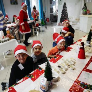Dzieci w czapkach Mikołaja przy stole czekają na warsztaty
