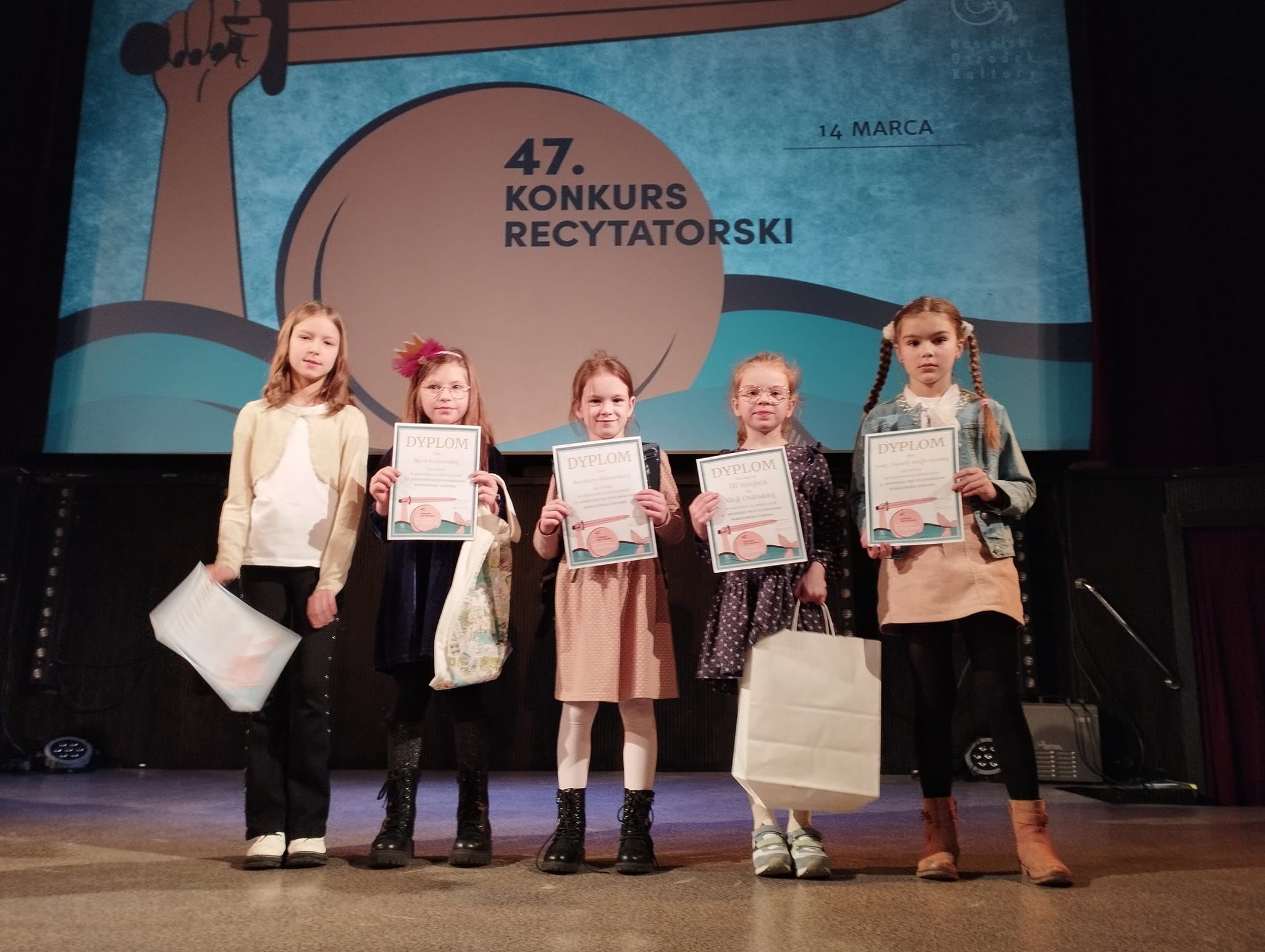 Dziewczynki z klas 1-3 na tle plakatu konkursu "Warszawska Syrenka"